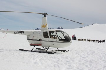 Helicopter landed on a glacier with sled dogs in the background